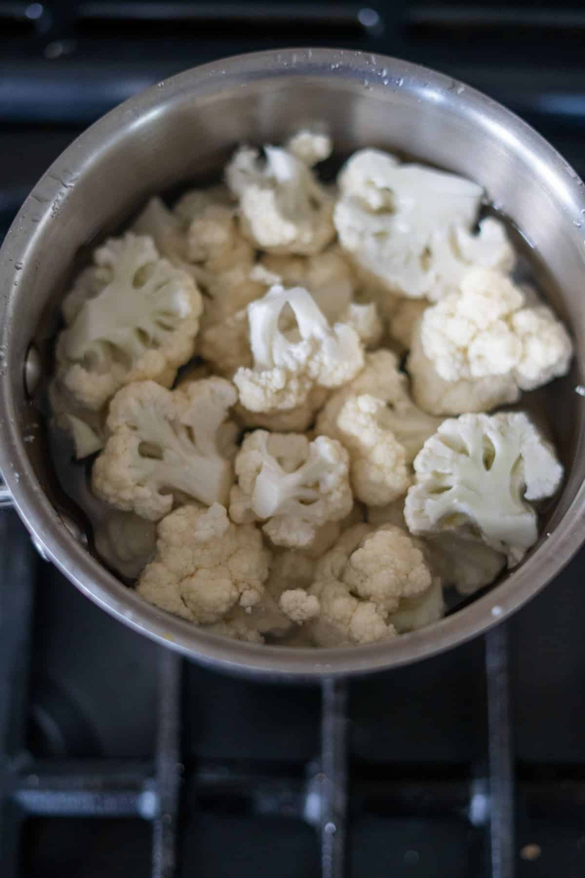 A pot of cauliflower florets, destined for a delicious low carb cauliflower bake, sits submerged in water on the stovetop.