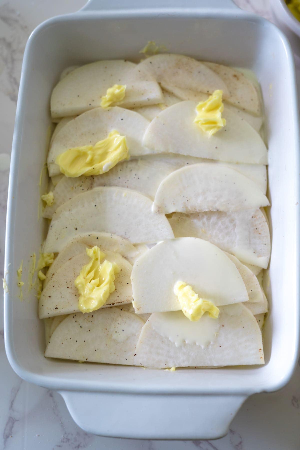 Sliced potatoes in a baking dish with butter, baked to perfection for a delicious turnip gratin.