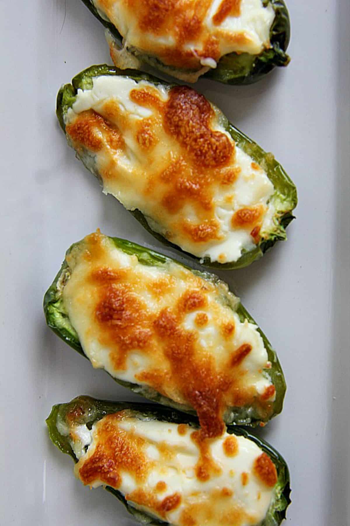 Four stuffed jalapeño halves filled with melted cheese, arranged in a vertical line on a white plate.