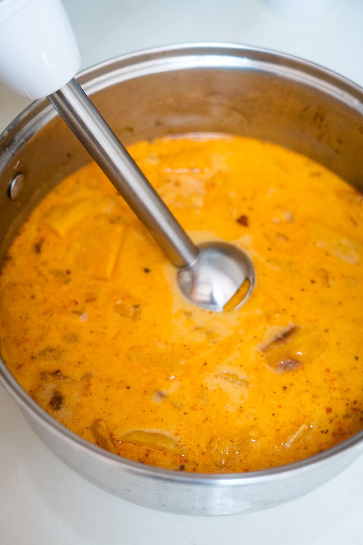A pot of butternut squash soup being stirred with a metal spoon.