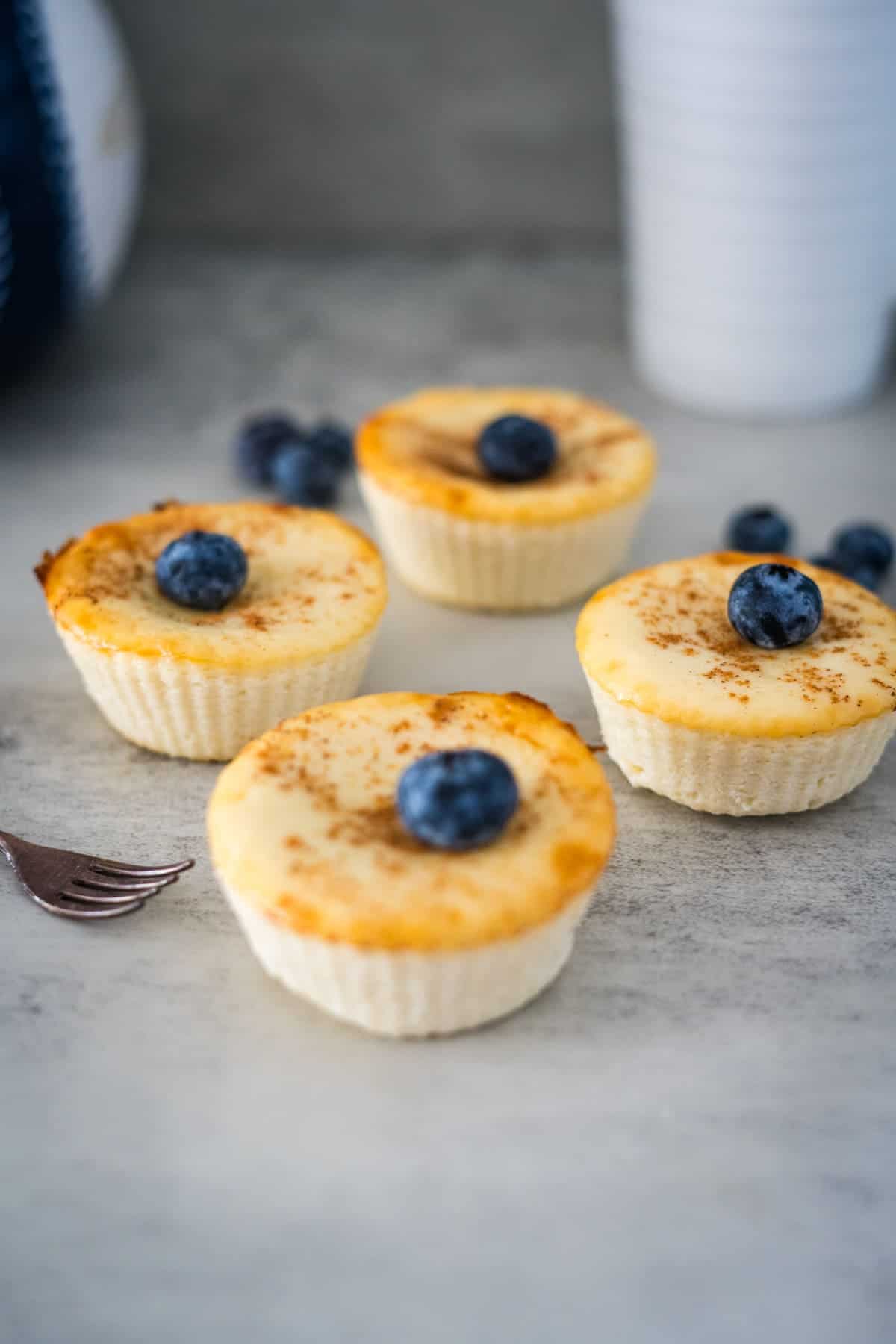 Four mini cream cheese muffins with blueberries on a table.
