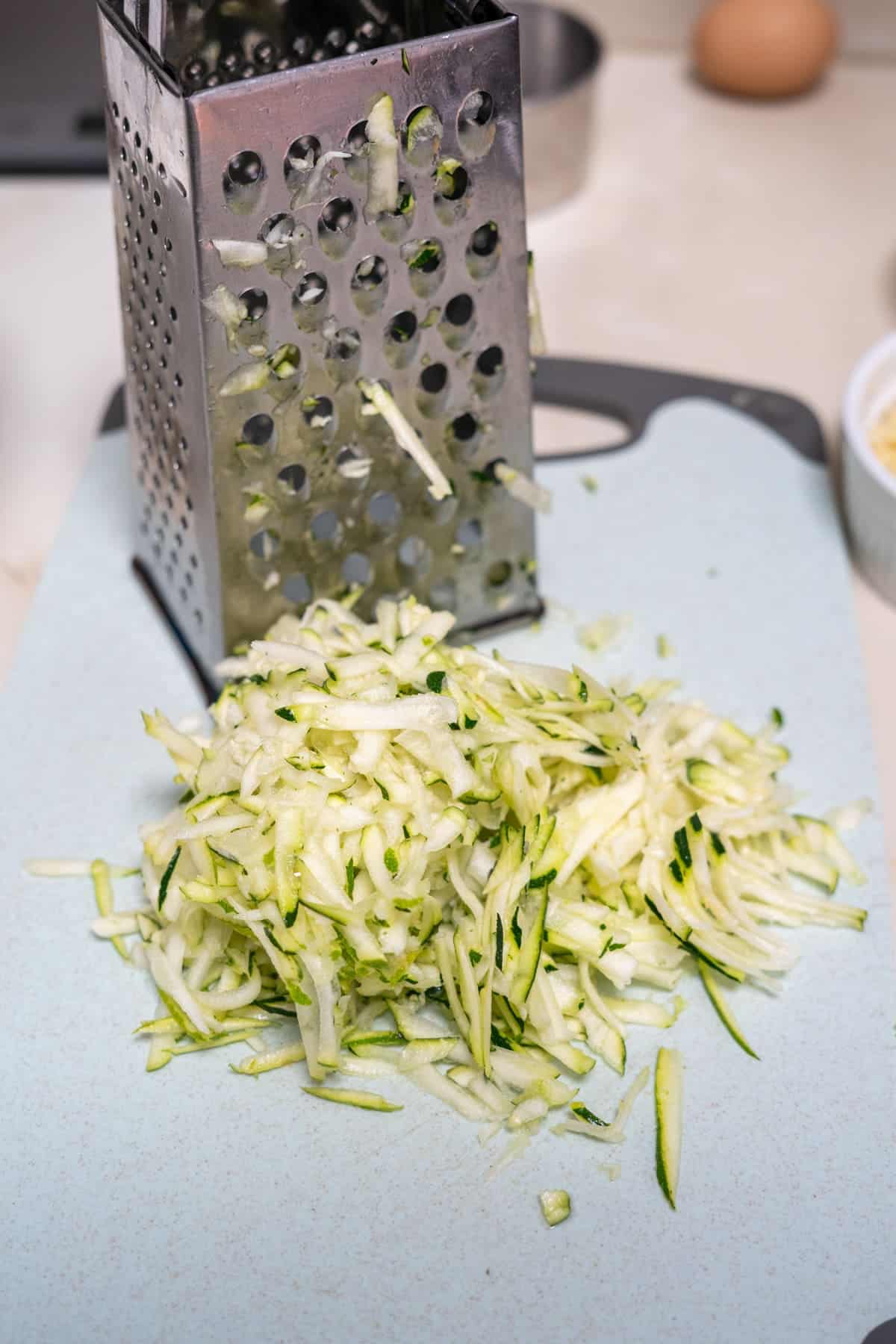 Shredded zucchini on a cutting board next to a box grater, perfect for crafting delicious keto zucchini nachos.