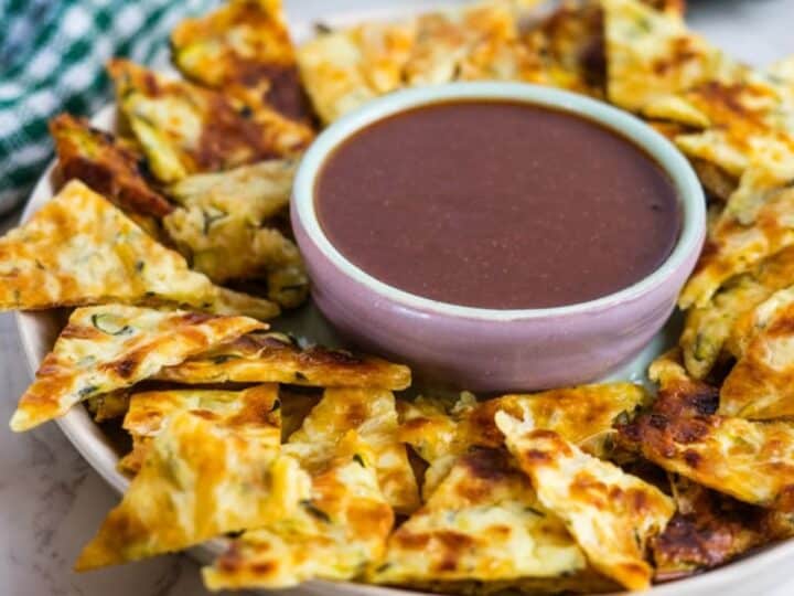 A platter of sliced cheesy garlic zucchini bread arranged in a circle around a bowl filled with marinara sauce, reminiscent of keto zucchini nachos.