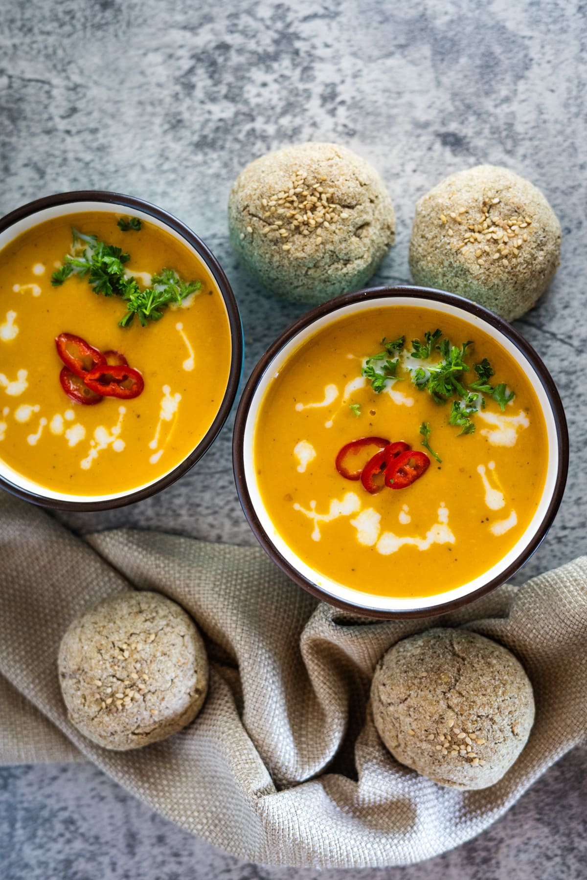 Two bowls of Thai butternut squash soup with bread on a table.