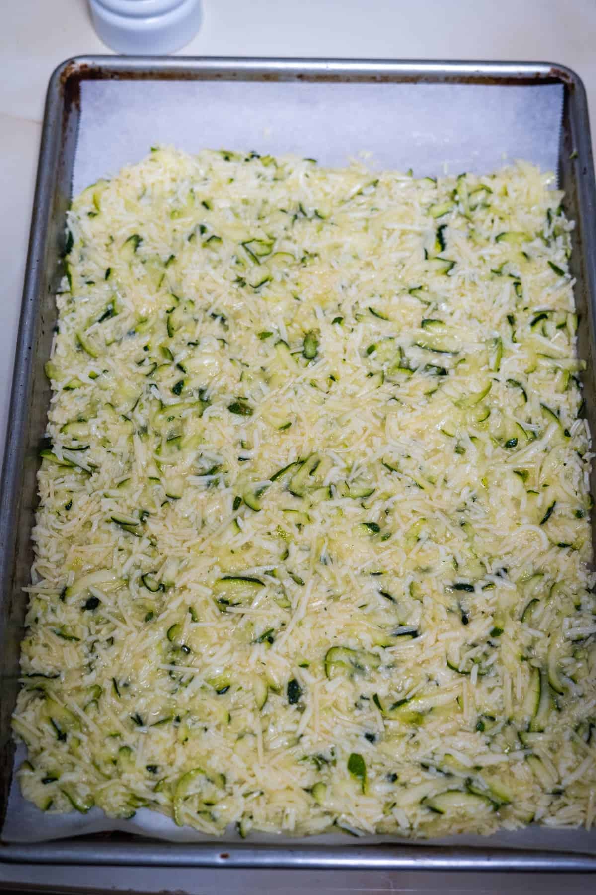 A baking tray filled with a mixture of shredded zucchini and cheese, ready to be cooked into delicious keto zucchini nachos.