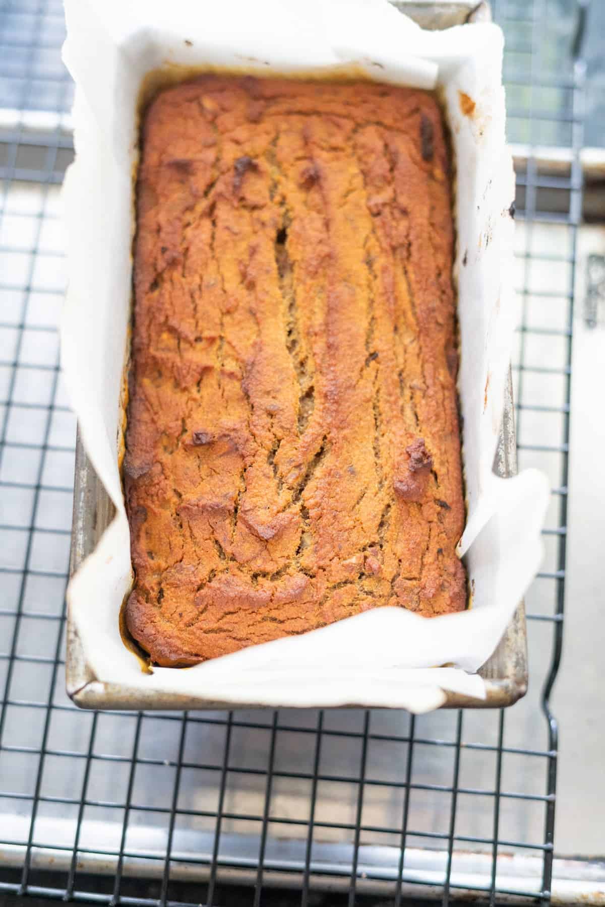 A loaf of keto pumpkin bread in a parchment-lined loaf pan, resting on a wire cooling rack.