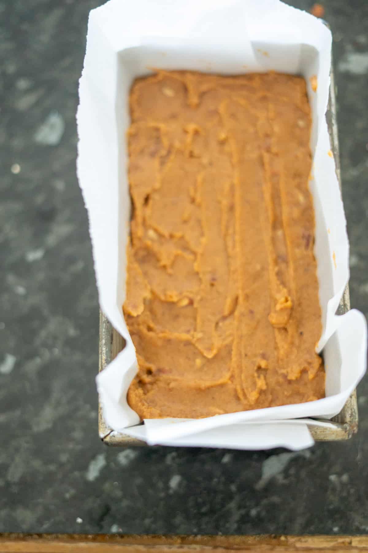 A rich, keto pumpkin bread batter spread smoothly in a parchment-lined loaf pan on a dark countertop.