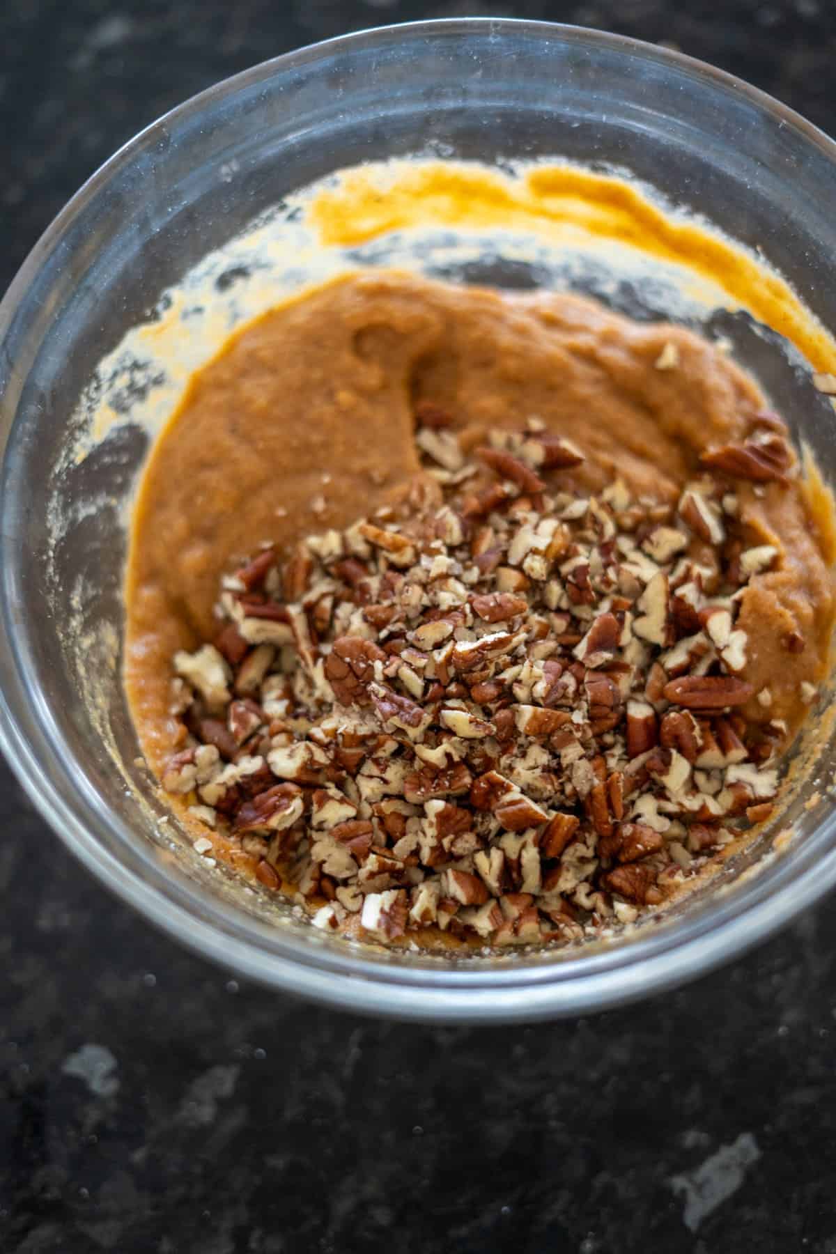 Bowl of keto pumpkin bread batter with chopped nuts on top, ready to be mixed.