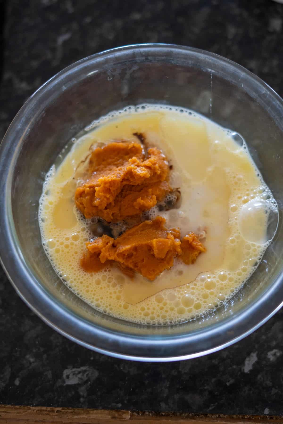 A glass bowl on a dark countertop holds a mix of pumpkin puree and wet ingredients, the perfect start for crafting delicious keto pumpkin bread.