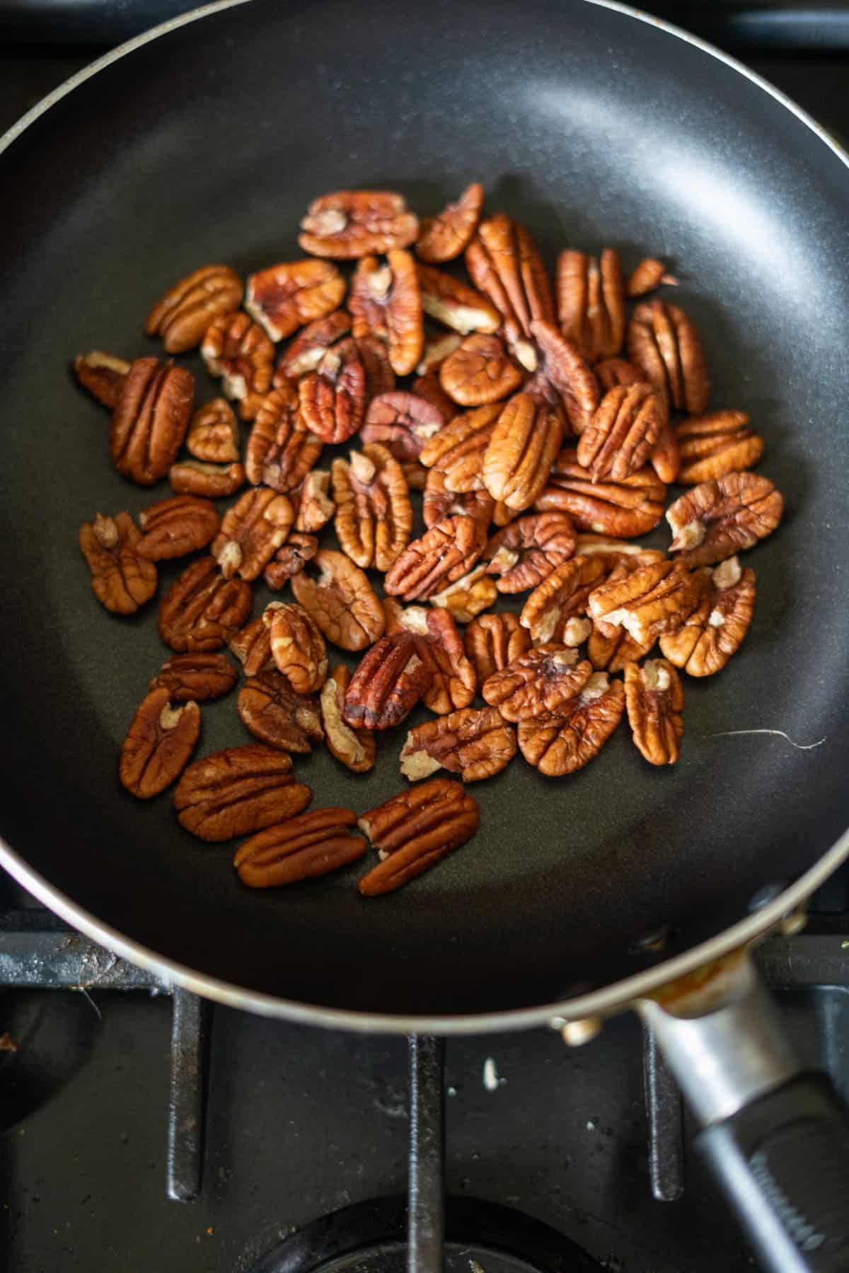 Pecan halves toast in a frying pan over a gas stove, adding the perfect crunch to your keto pumpkin bread creation.