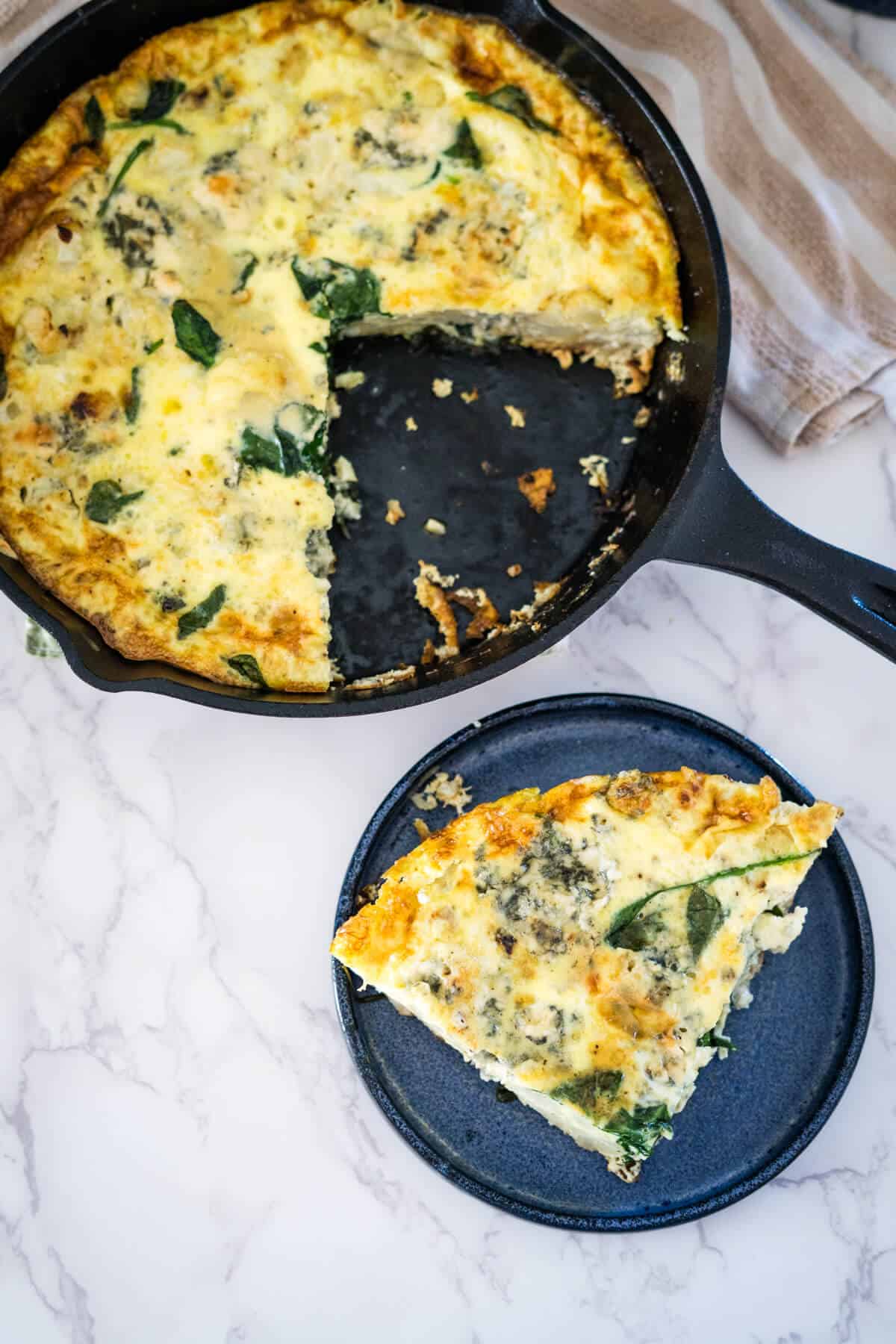 A skillet with a slice of frittata and spinach on it.