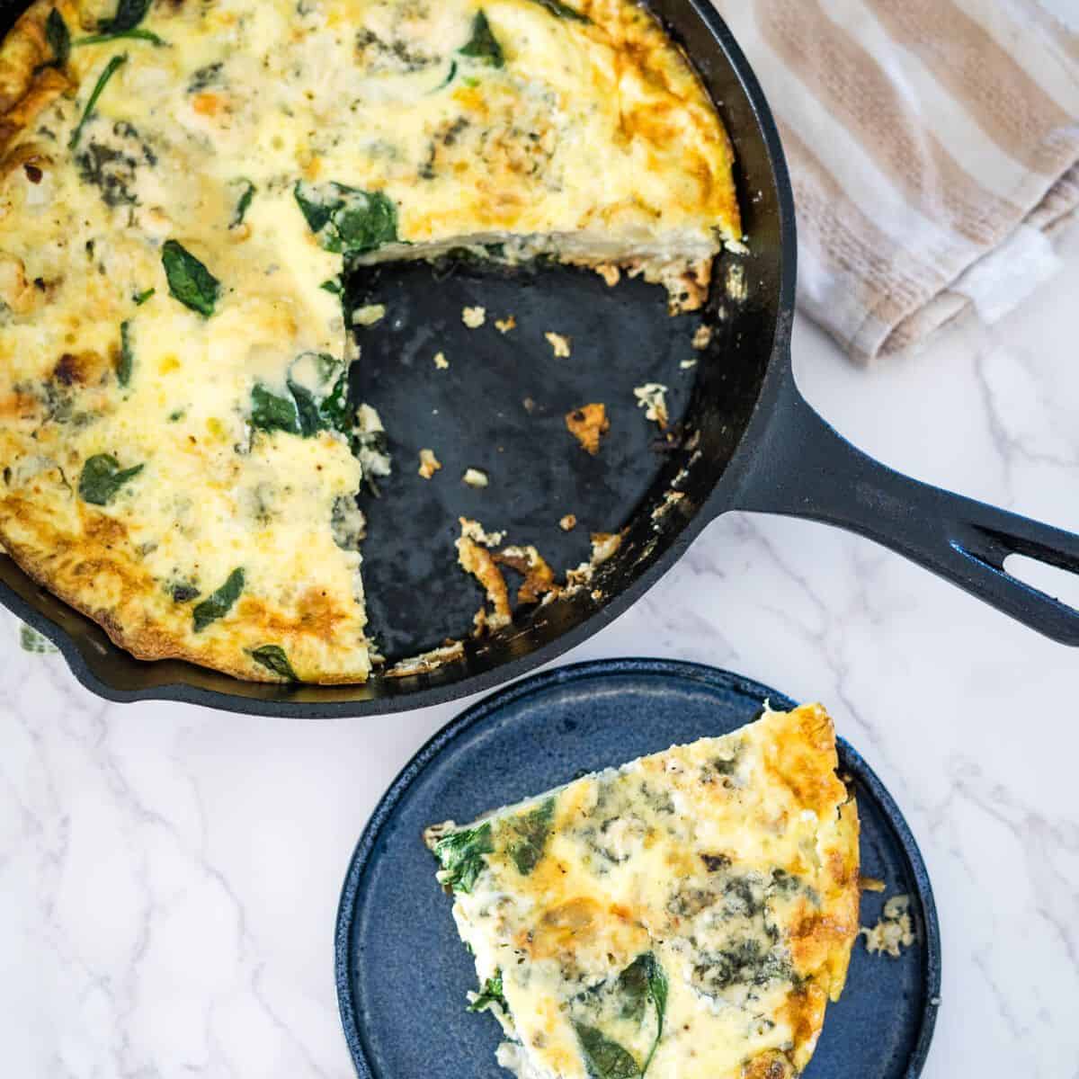 A skillet full of spinach and cheese frittata with a slice taken out.
