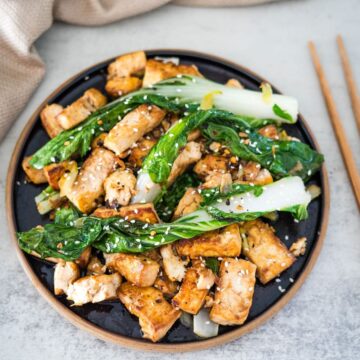 Tofu stir fry with greens and chopsticks on a plate.