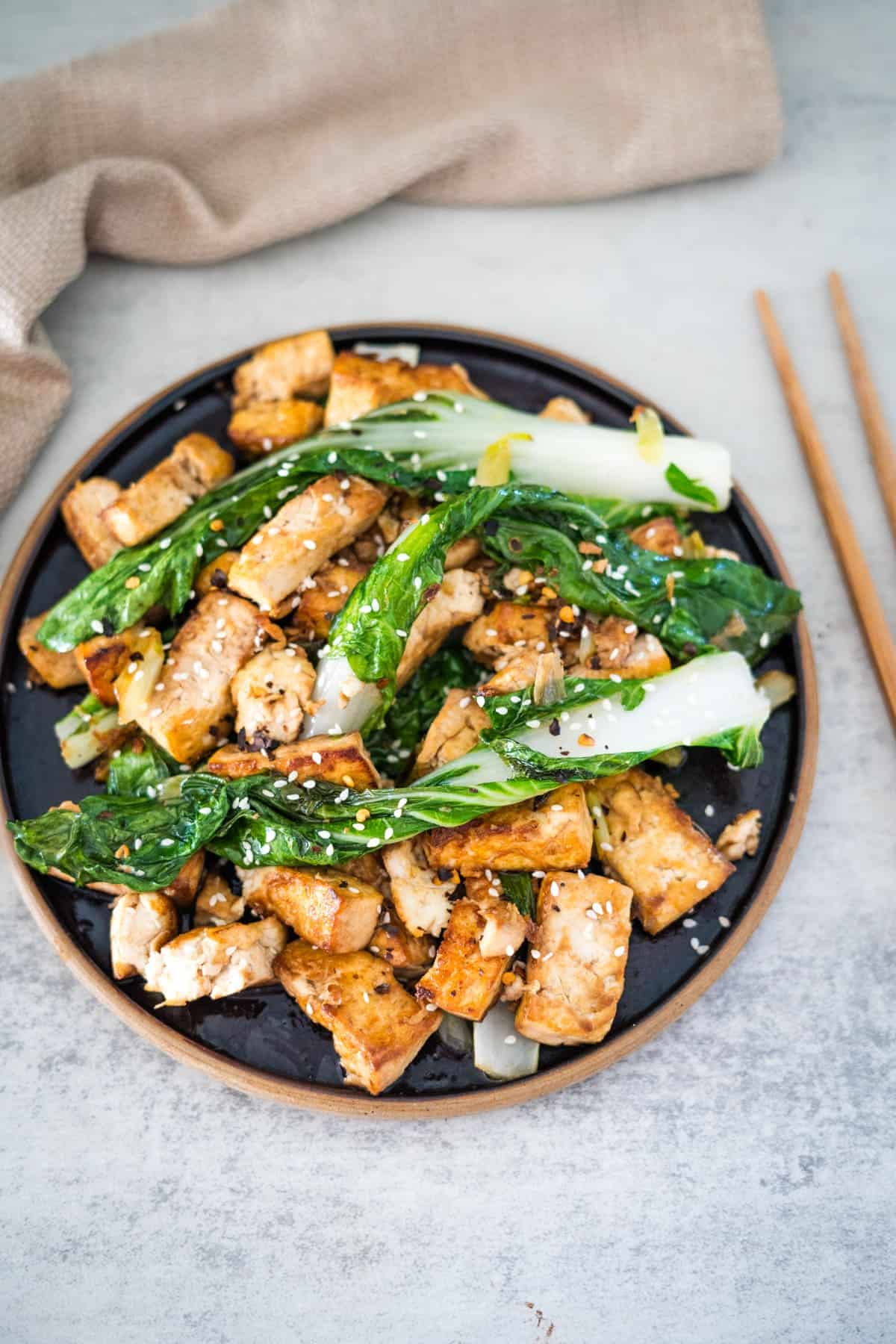 Tofu and greens on a plate with chopsticks.