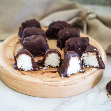 Bounty bars rest on a wooden plate, some cut open to reveal their chocolate-covered coconut filling.