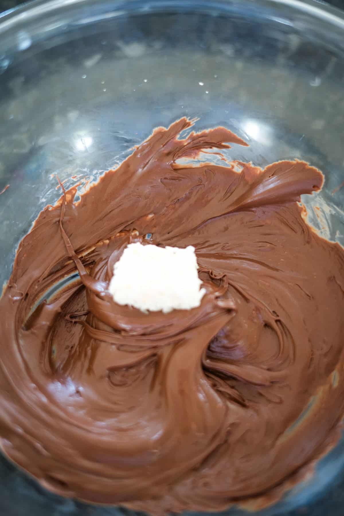 A glass bowl containing melted chocolate with a small piece of butter on top, reminiscent of the sweet allure of bounty bars.