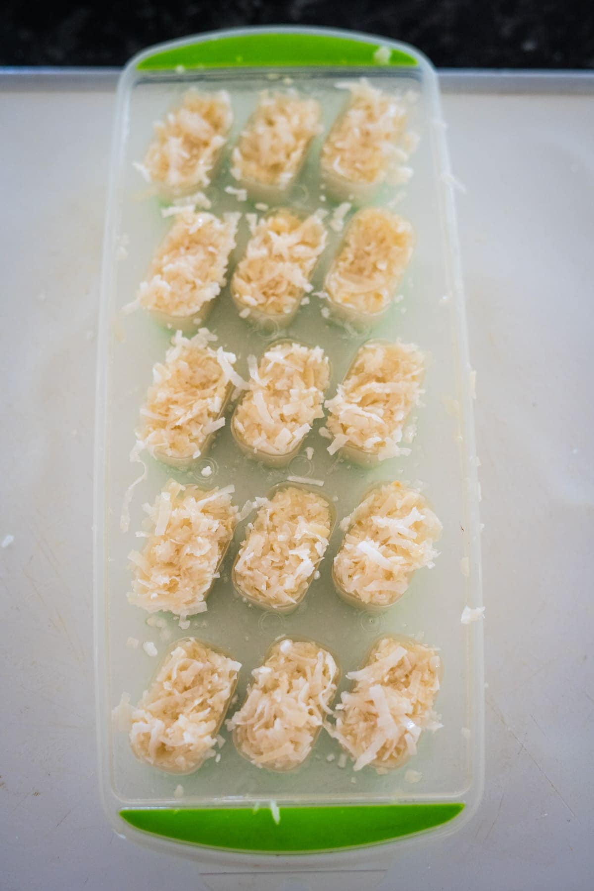 Close-up of a green ice cube tray filled with a shredded coconut mixture reminiscent of the classic bounty bars.