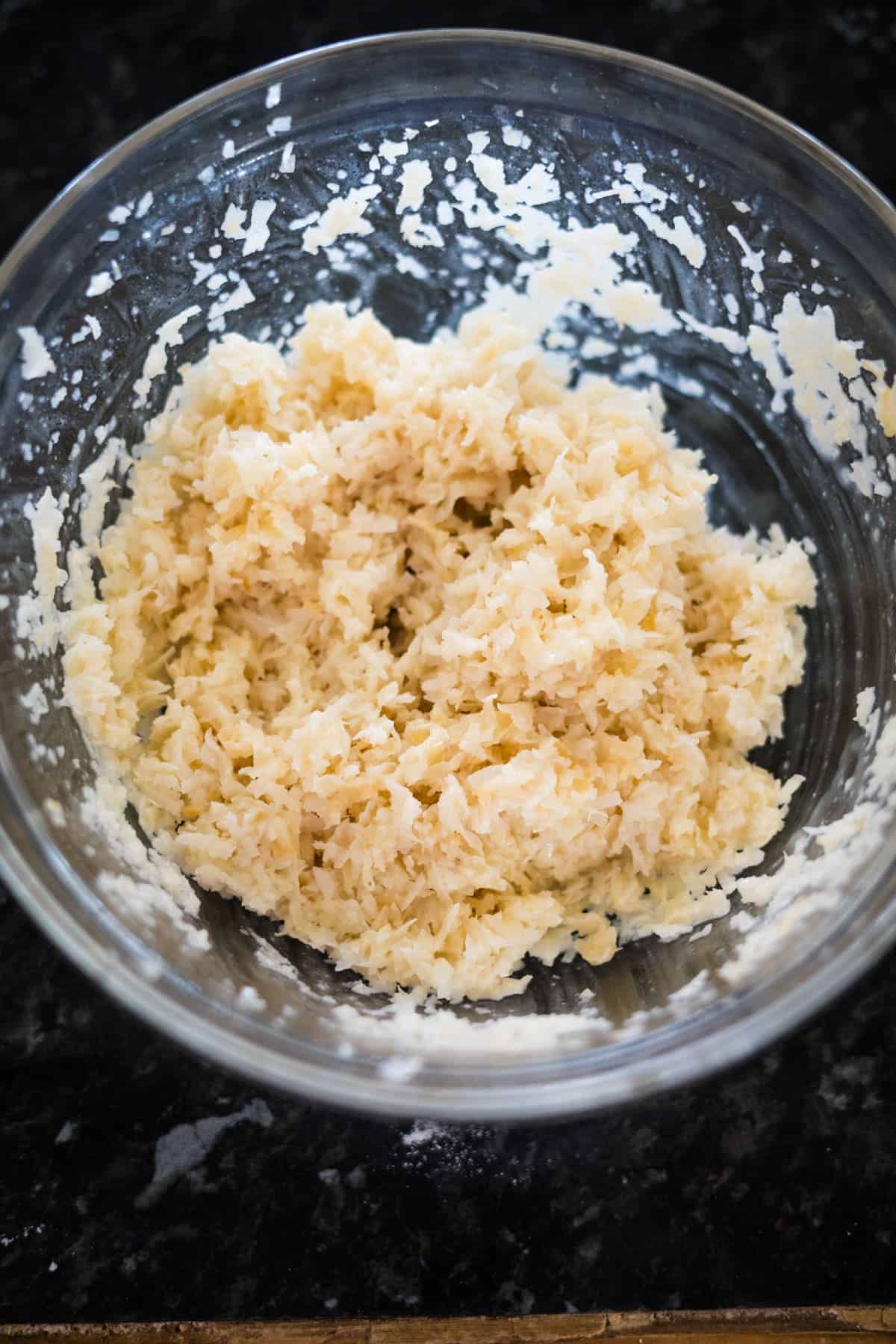 A glass bowl containing a mixture of grated Parmesan cheese and shredded coconut sits like the essence of homemade bounty bars on a dark surface.