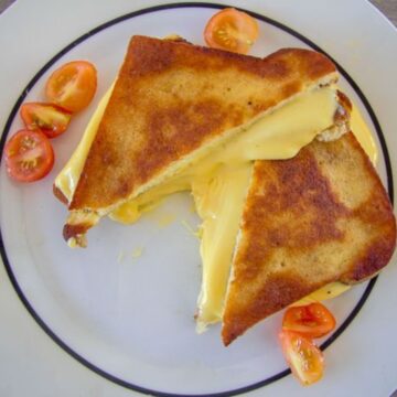 Two halves of a keto grilled cheese sandwich with melted cheese, garnished with sliced cherry tomatoes, on a white plate.