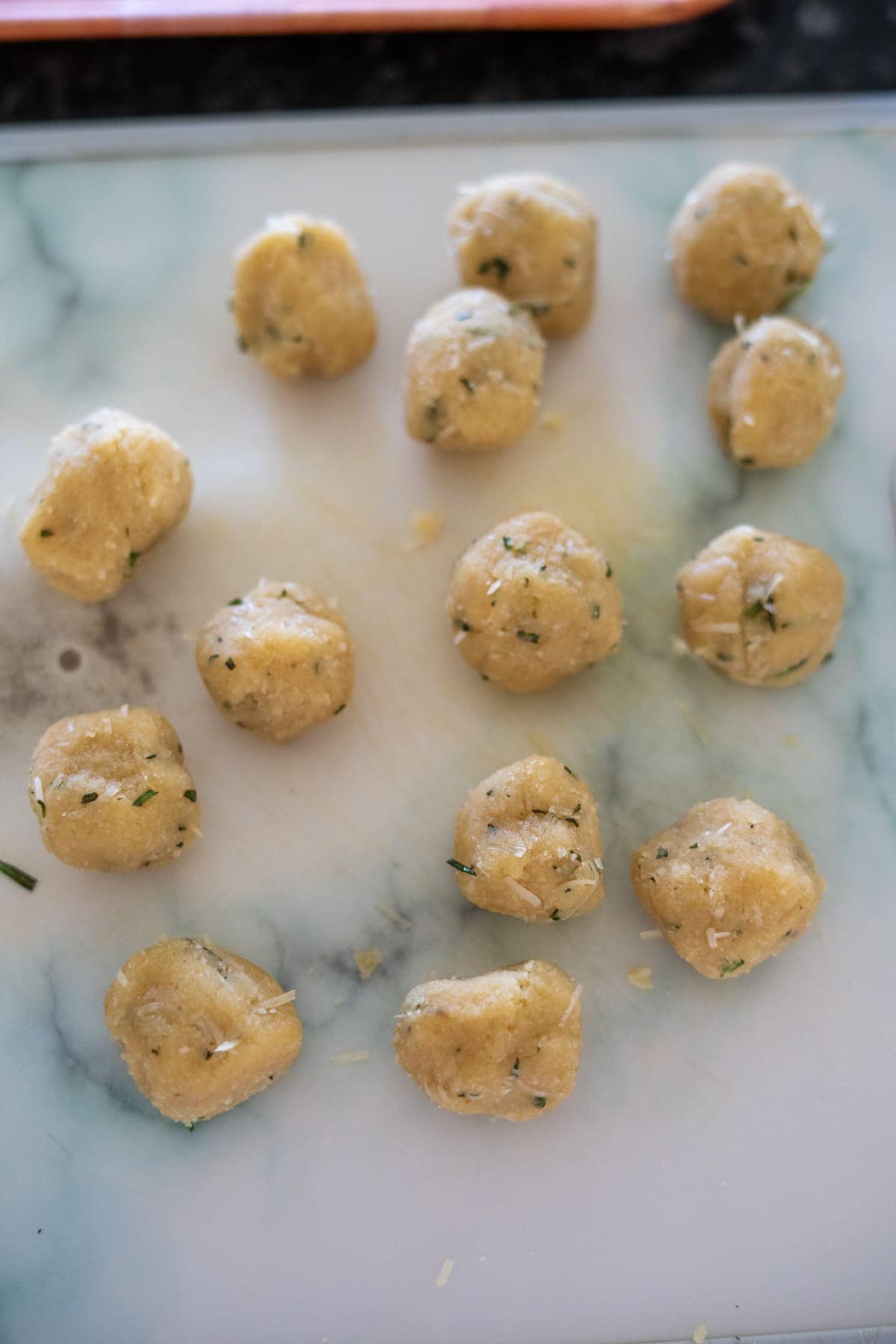 Sixteen uncooked dough balls infused with rosemary and Parmesan sit on a marble surface.