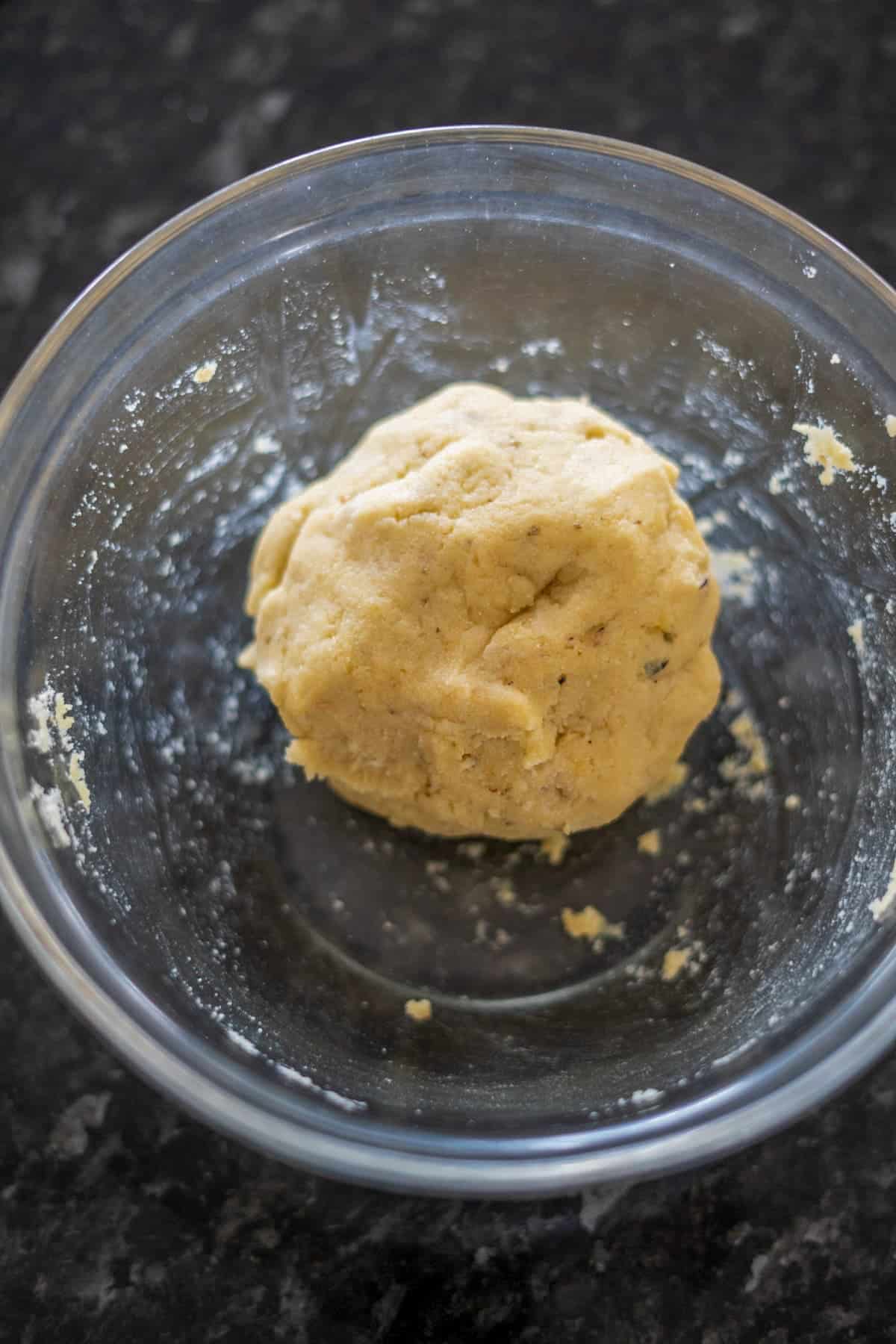 A ball of dough, enriched with almond flour, rests in a clear glass bowl on a dark countertop.