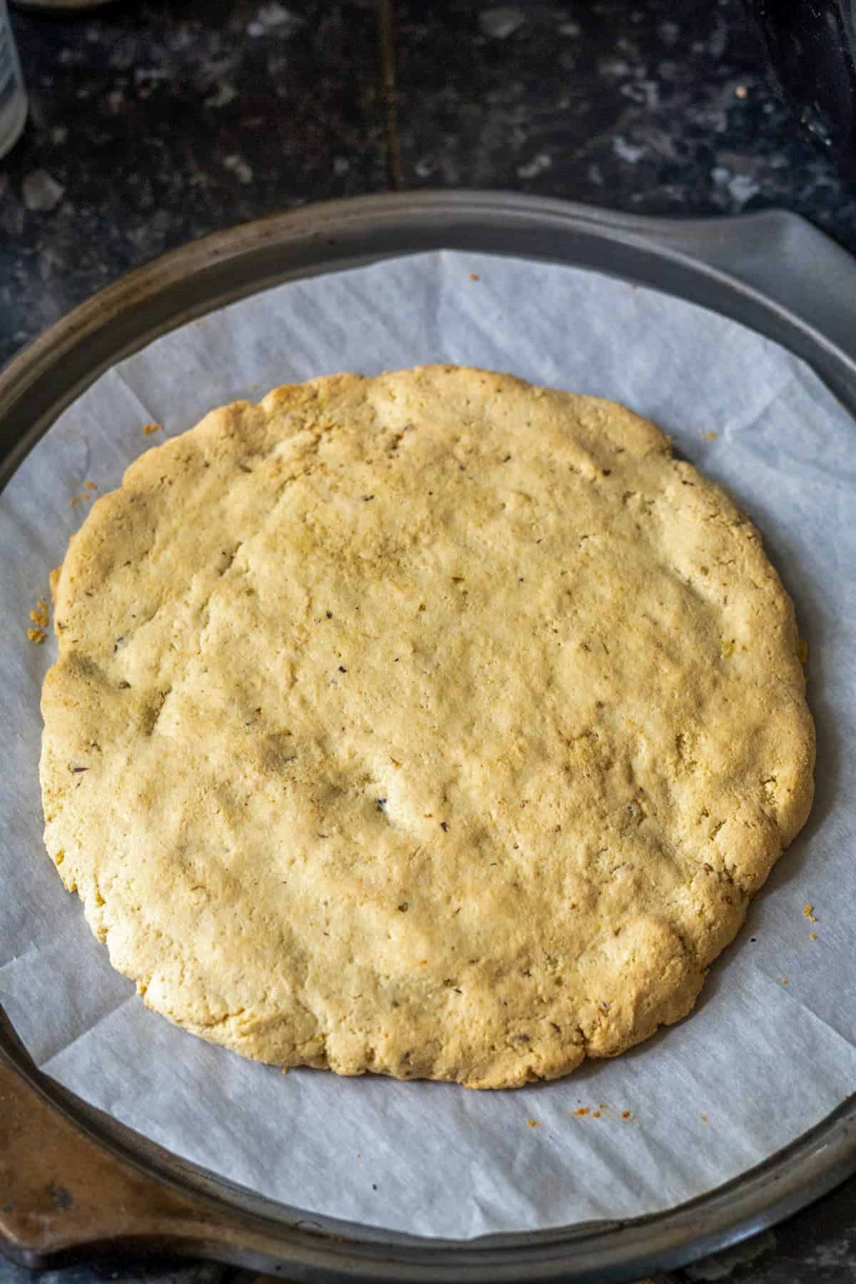 A round, golden-brown dough made with almond flour rests on parchment paper on a baking tray.