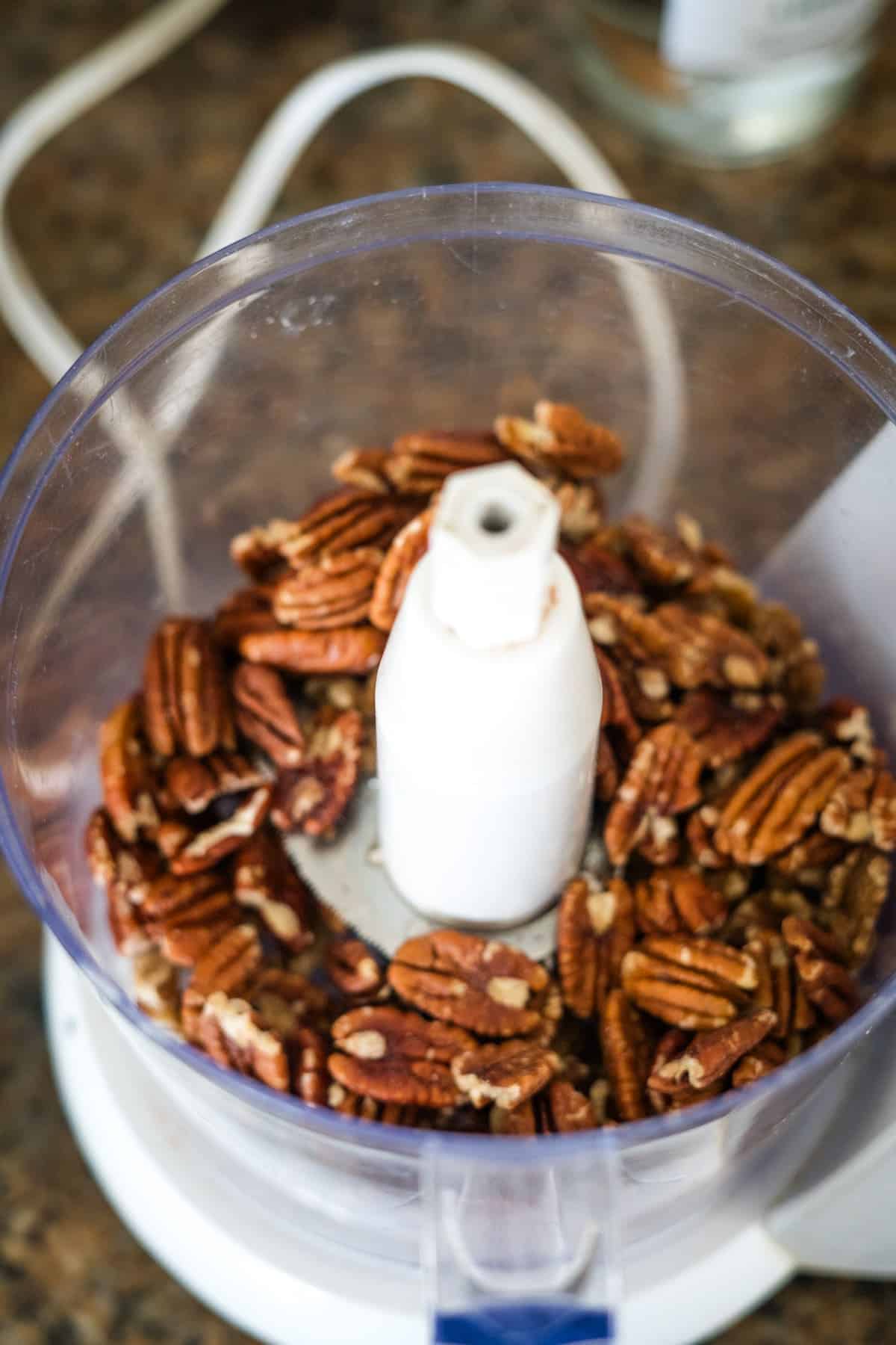 Pecans in a food processor ready to be chopped for keto berry tarts, placed on a kitchen countertop.