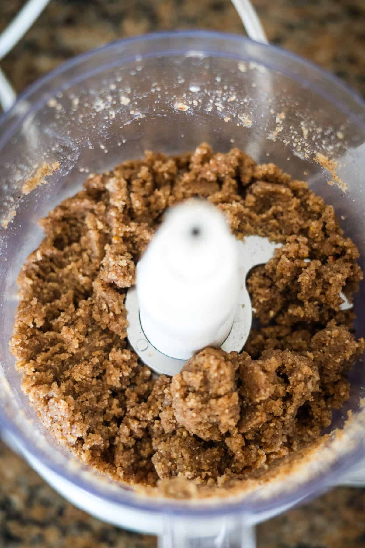 Close-up of a food processor filled with a coarse, grainy mixture resembling cookie dough, viewed from above, perfect for creating keto berry tarts.