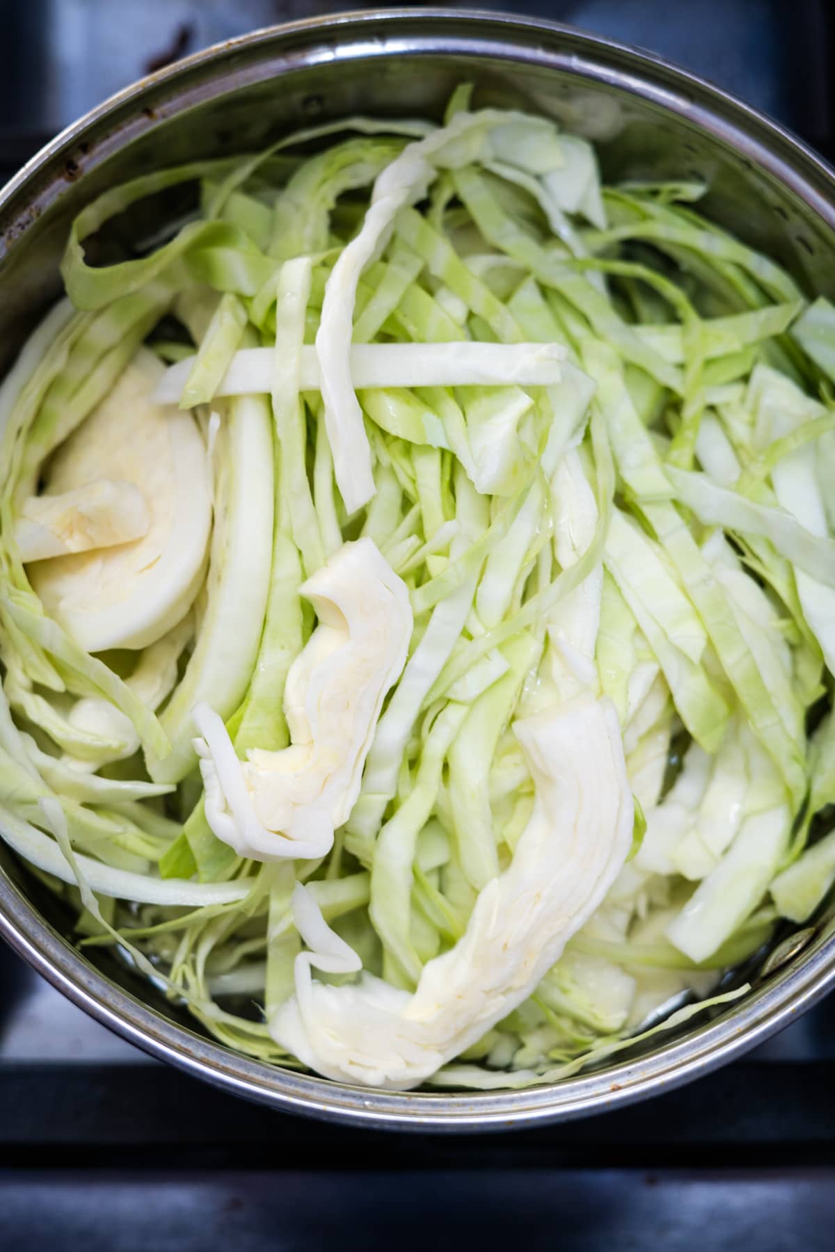 Sliced cabbage in a pan on a stove.