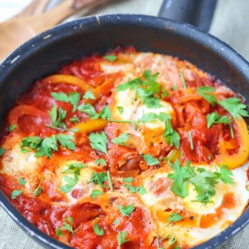 A shakshuka with poached eggs in a tomato and bell pepper sauce garnished with fresh parsley.