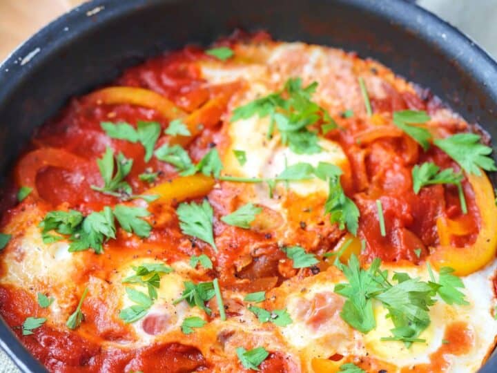 A shakshuka with poached eggs in a tomato and bell pepper sauce garnished with fresh parsley.