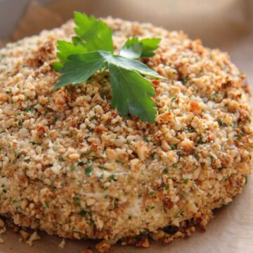 Round baked Camembert ball coated in crushed nuts and parsley, garnished with a sprig of parsley on top.