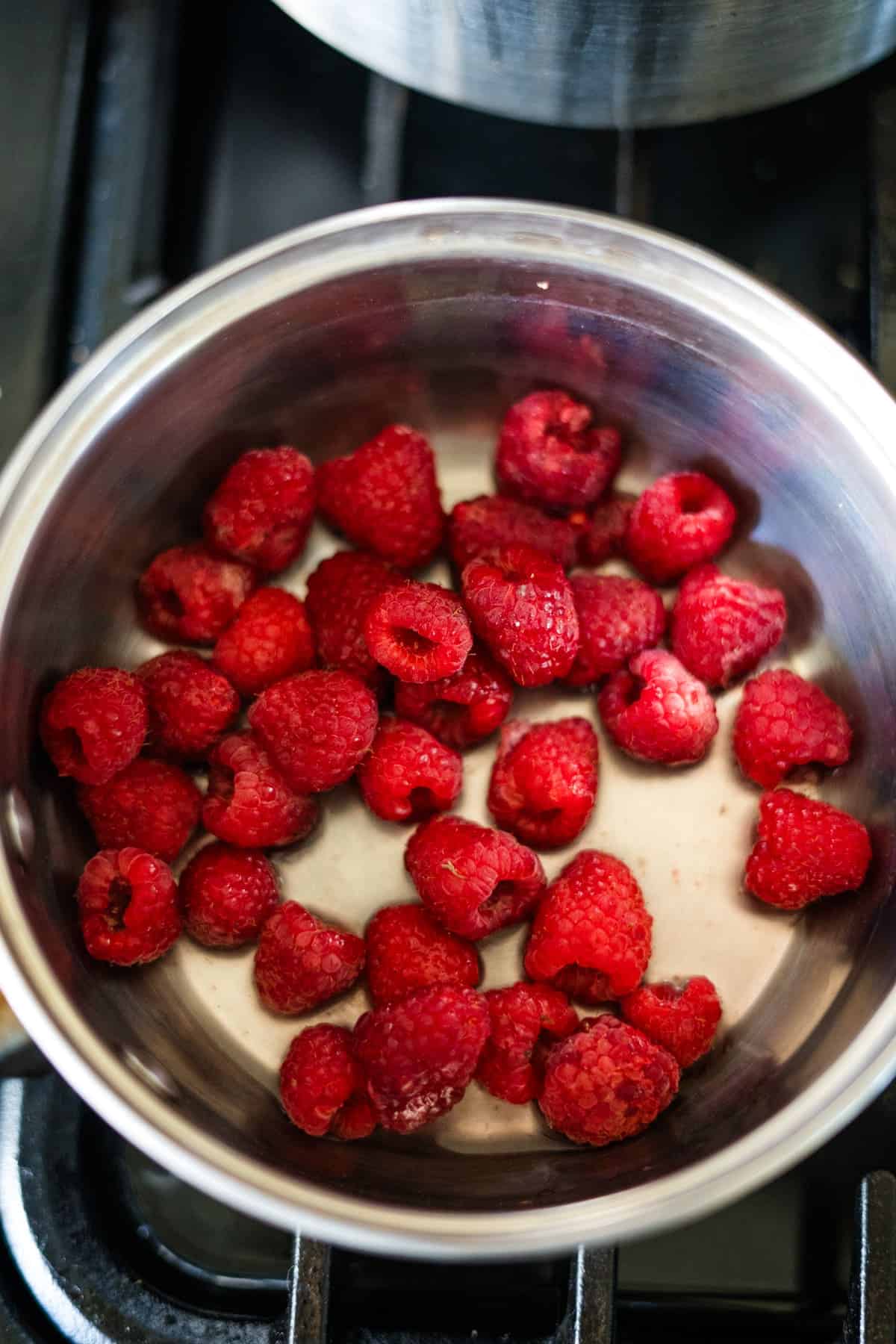 A stainless steel pot filled with fresh red raspberries sits on a stovetop, ready to be transformed into luscious raspberry chia jam.