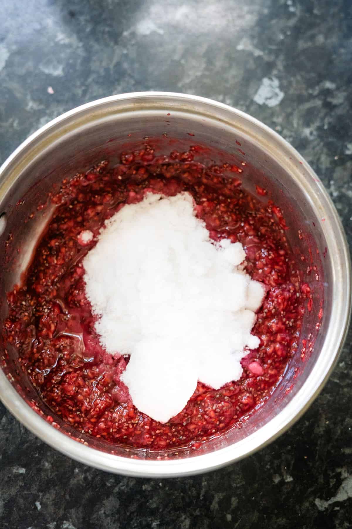 Stainless steel pot containing a mixture of crushed raspberries, chia seeds, and sugar, creating a delightful raspberry chia jam.