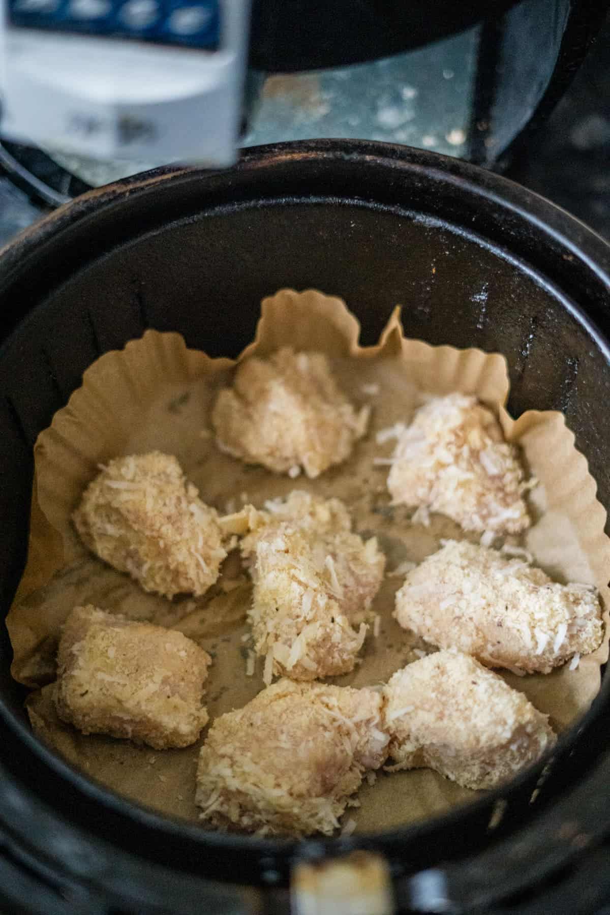 Chicken bites covered in a breadcrumb coating are lined up inside an air fryer with parchment paper at the bottom.