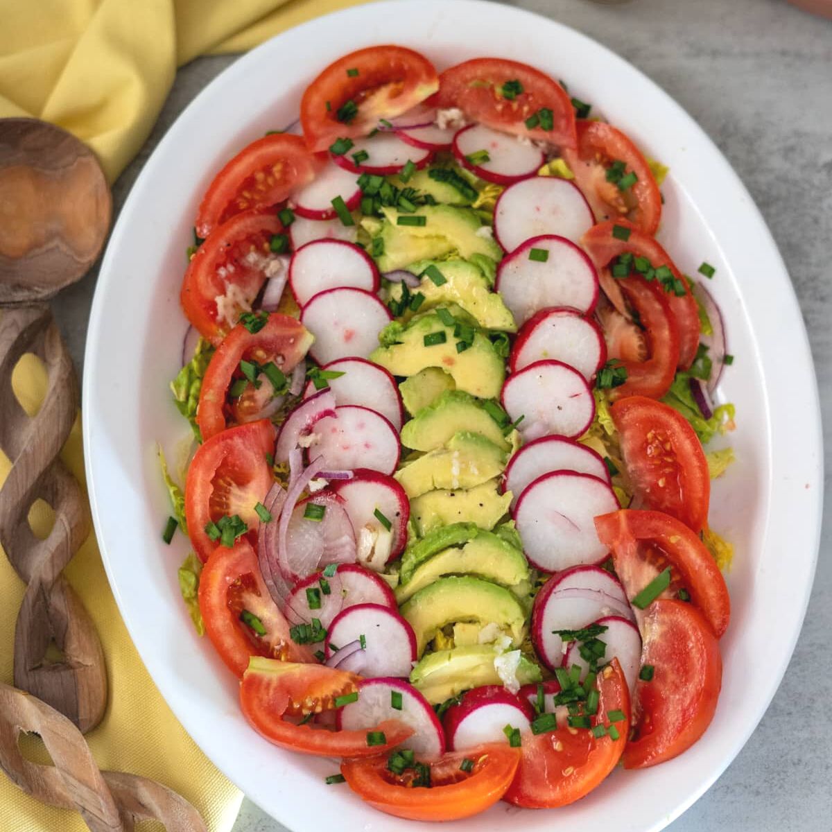A mixture of tomato, radishes, avocado and red onion arranged on an oval plate.