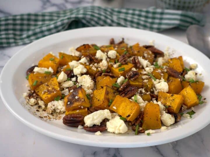 Roasted pumpkin with feta and pecans on a white plate.