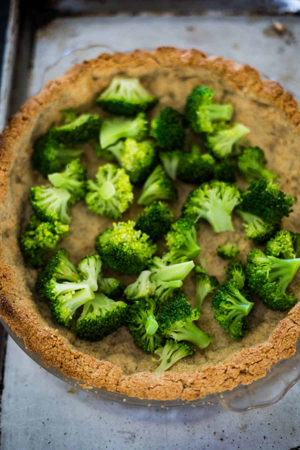 A close-up of a pie crust filled with broccoli florets, ready to be baked into a delicious broccoli and blue cheese quiche.