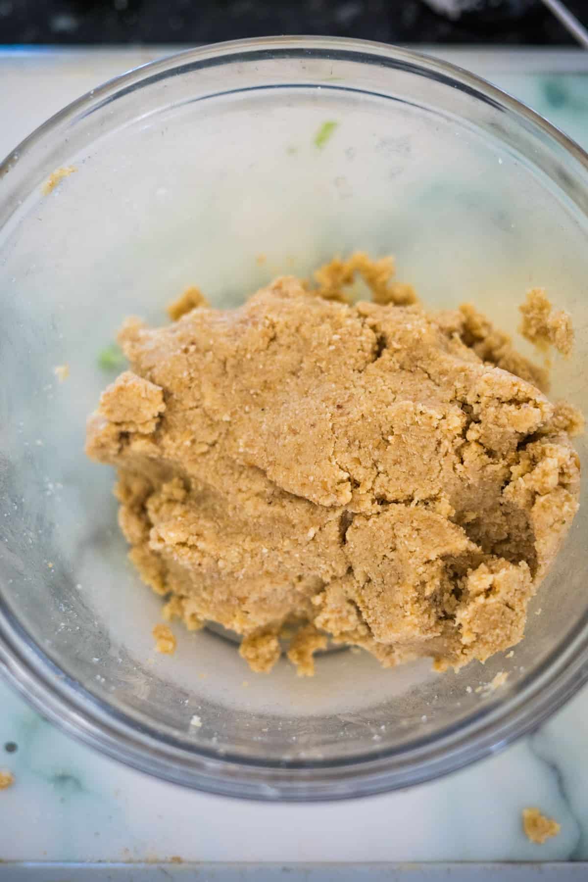 A glass bowl containing beige-colored dough sits on a light-colored surface, ready to be transformed into a delicious broccoli and blue cheese quiche.