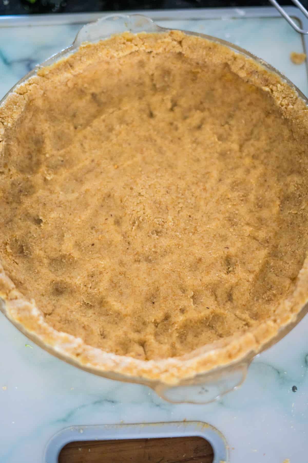 A homemade pie crust in a glass pie dish on a marble-like background, ready for filling with a delicious broccoli and blue cheese quiche.