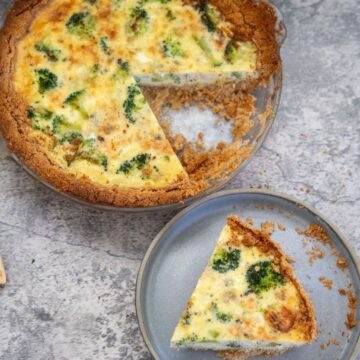 A broccoli and blue cheese quiche with a slice removed, placed on a separate plate next to it. The quiche filling includes broccoli and melted cheese, and the crust is golden brown.