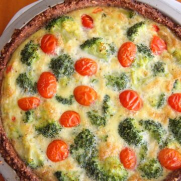 Freshly baked quiche with a broccoli crust and cherry tomatoes visible on top, served in a round dish.