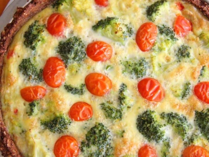 Freshly baked quiche with a broccoli crust and cherry tomatoes visible on top, served in a round dish.