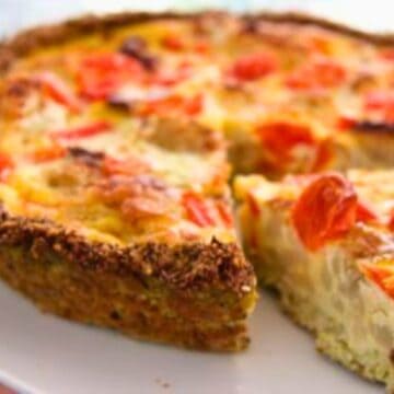 A slice of tomato, cauliflower, and zucchini quiche on a white plate, with visible herbs and a golden-brown crust.