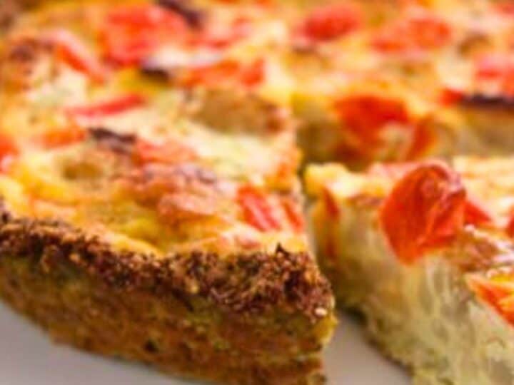 A slice of tomato, cauliflower, and zucchini quiche on a white plate, with visible herbs and a golden-brown crust.