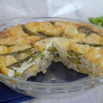 A glass pie dish showcasing a partially eaten crustless quiche, with visible green asparagus nestled in a golden-brown filling.