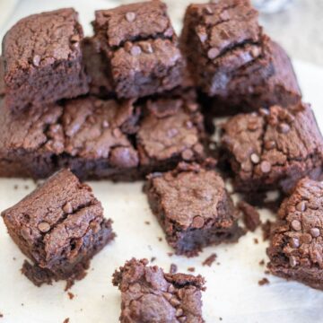 A stack of chocolate brownies with chocolate chips on top, placed on white parchment paper.