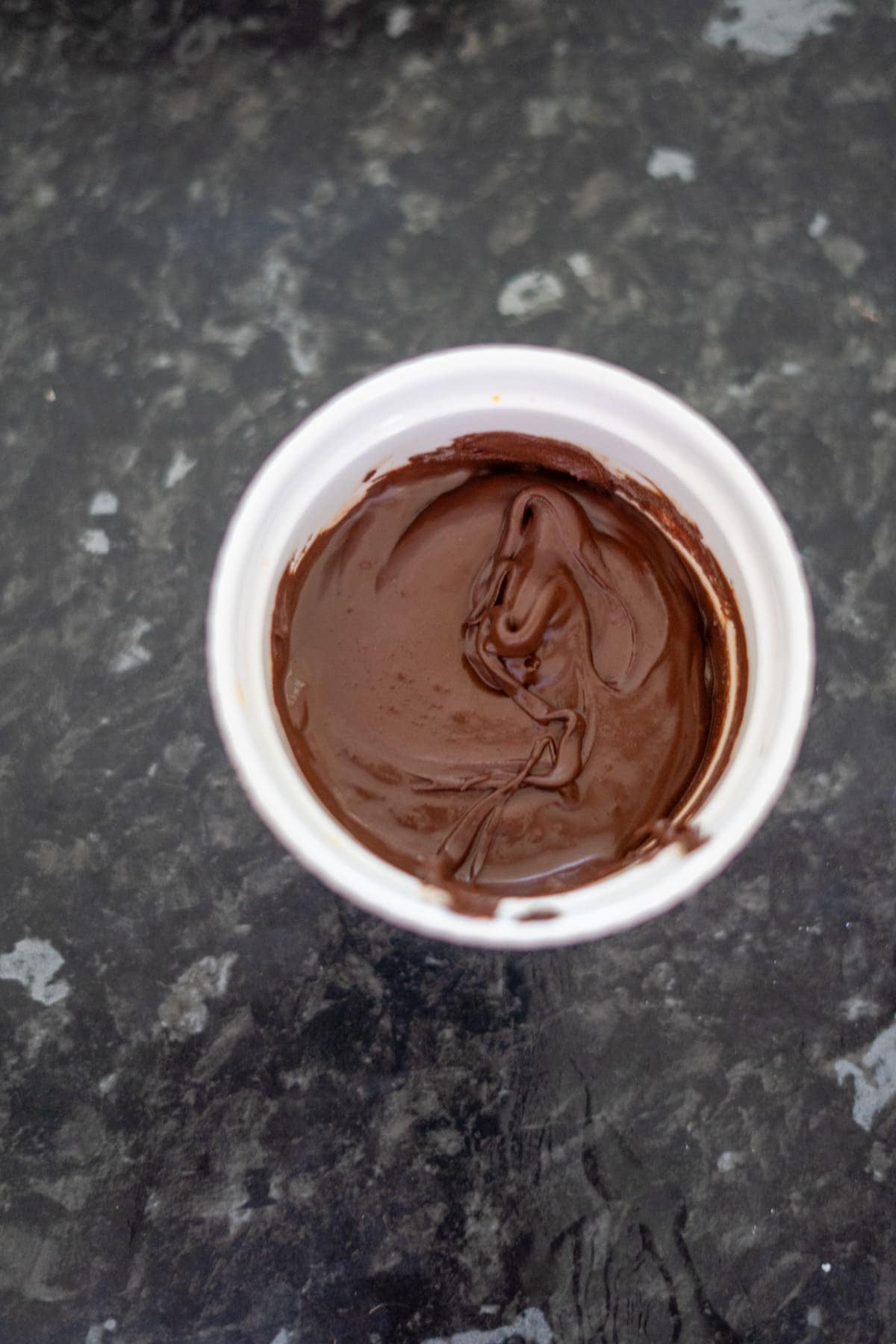 A white cup filled with smooth, melted chocolate on a dark marbled surface.