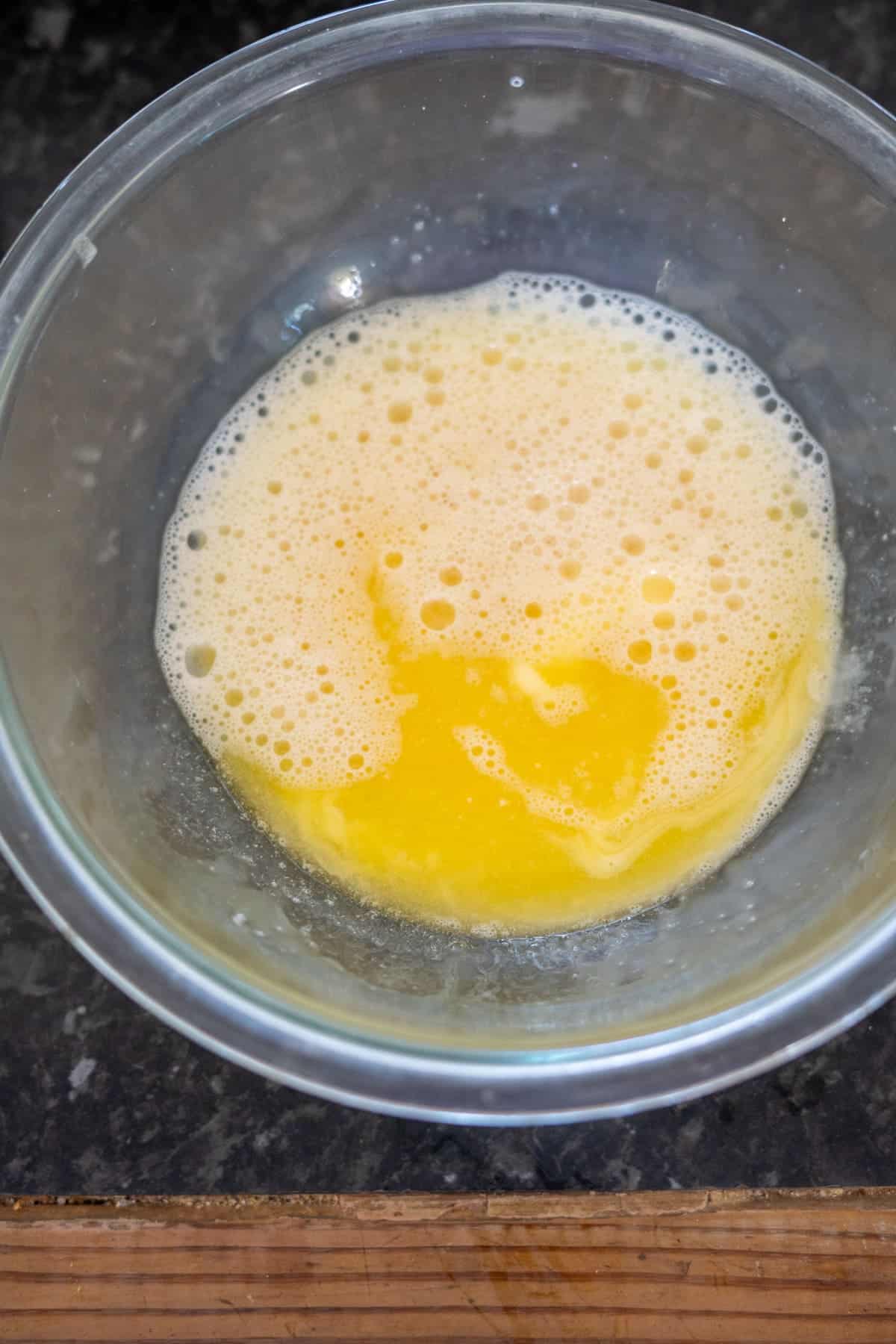 A glass bowl containing beaten eggs on a dark countertop.