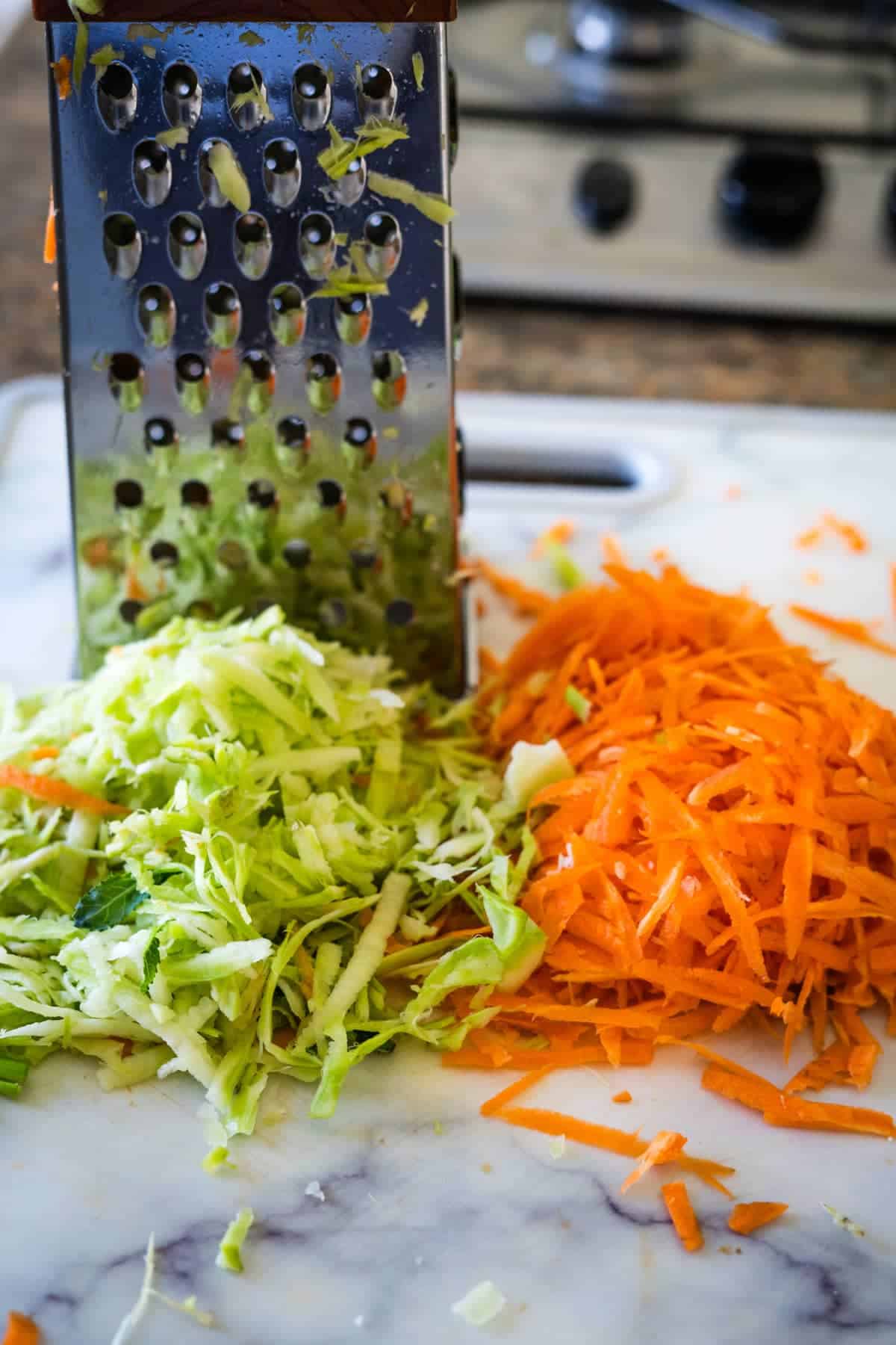 A grater on a cutting board with carrots and coleslaw.